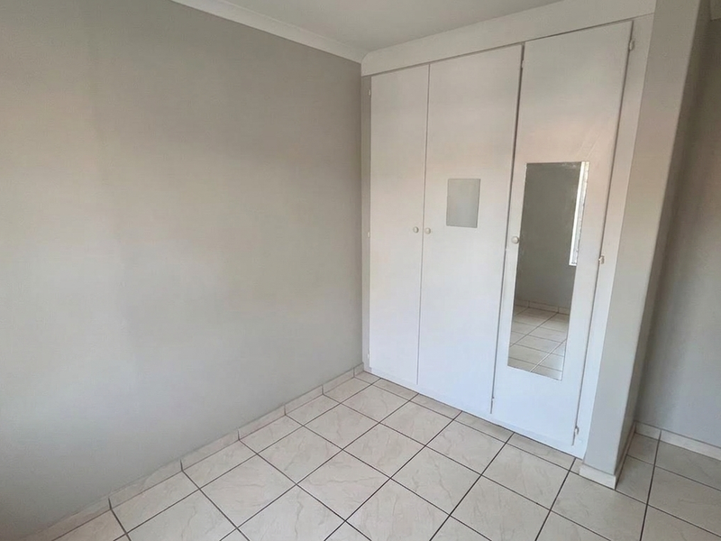 A clean, empty bedroom featuring neutral wall paint, tiled flooring, and built-in cupboards with a mirrored panel.