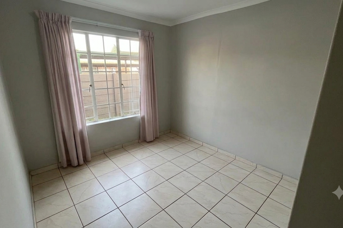 A clean, empty bedroom featuring neutral tiled flooring, coving, and a window fitted with security burglar bars.