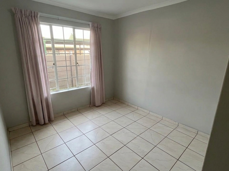 A clean, empty bedroom featuring neutral tiled flooring, coving, and a window fitted with security burglar bars.