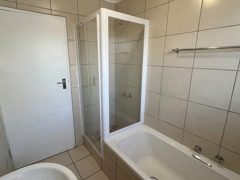 A functional bathroom featuring a bathtub, a separate shower enclosure, and neutral wall tiling throughout.
