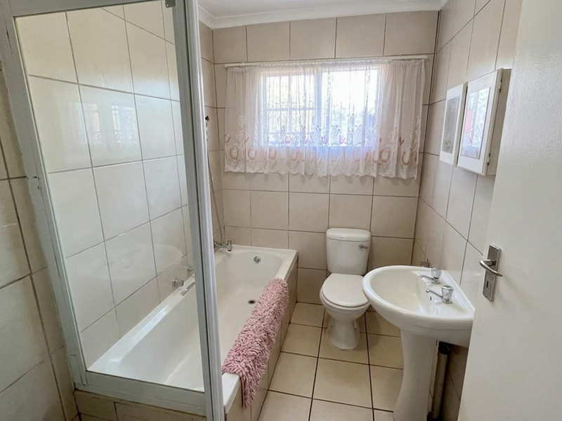 A functional bathroom featuring a bathtub with a shower screen, a pedestal basin, and a toilet, finished with neutral wall and floor tiles.