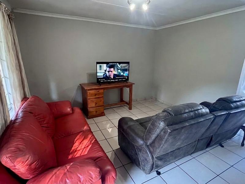 A living room featuring tiled flooring, neutral wall paint, and natural light through a window with security bars.