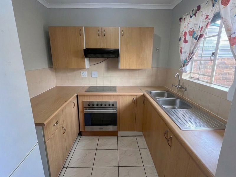 Functional kitchen featuring light wood-finish cabinetry, laminate countertops, built-in oven with hob, and a double stainless steel sink with tiled splashback.