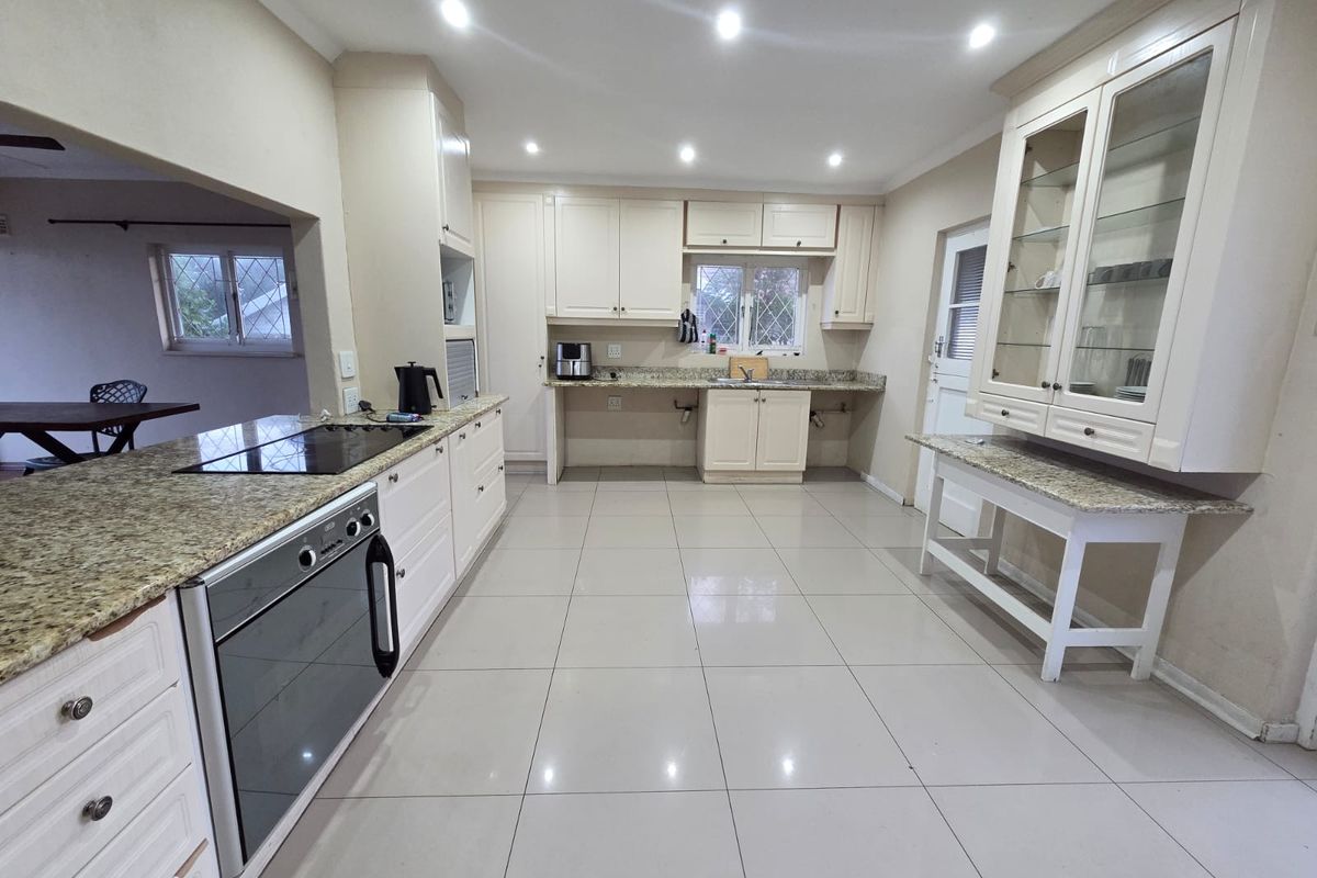 Spacious kitchen featuring granite countertops, built-in oven, electric cooktop, and ample cabinetry with integrated glass-fronted display units and tiled flooring.