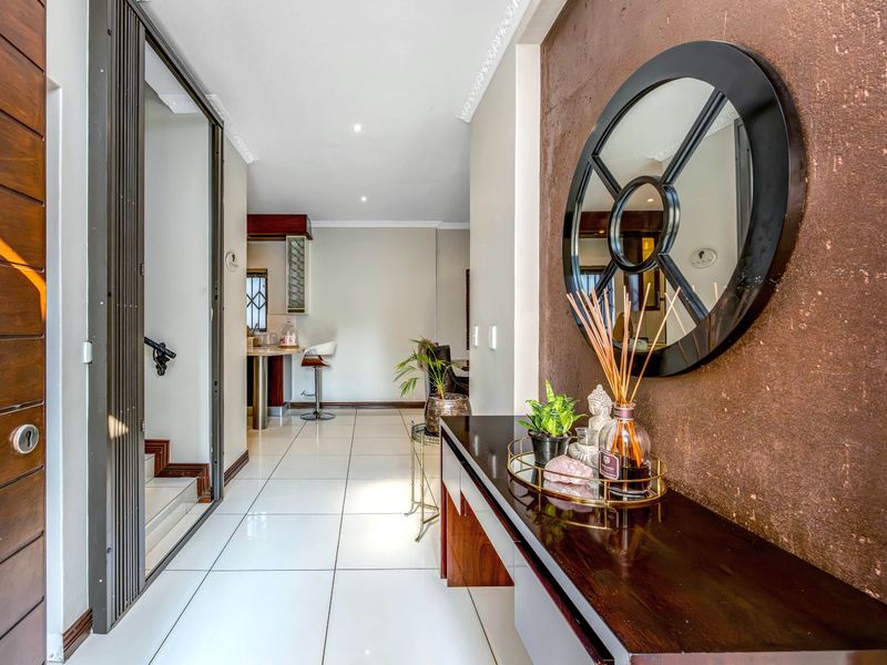 A bright and modern entrance hall featuring polished white floor tiles, crown molding, and a built-in console, leading towards the open-plan living area.