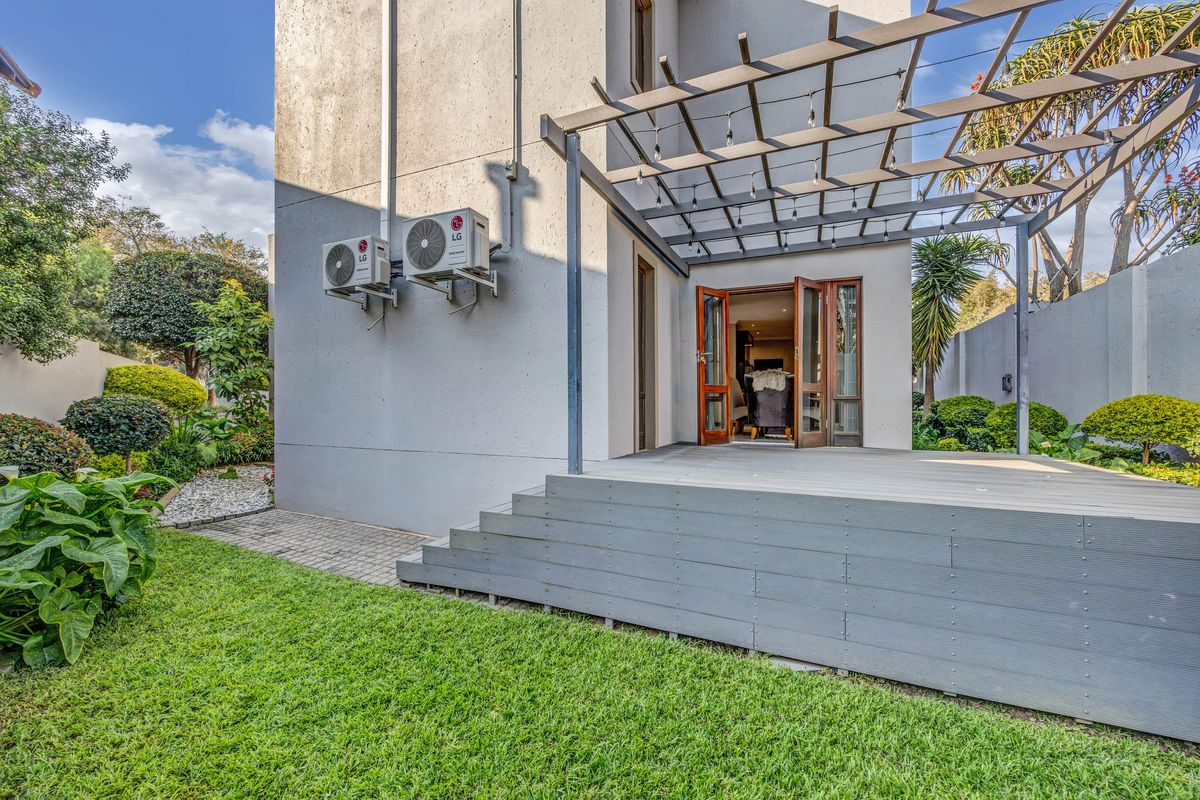 Rear exterior view featuring a raised timber deck with a pergola, landscaped garden, and dual air conditioning units mounted on the building facade.