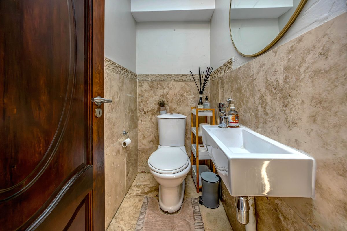 A compact guest bathroom featuring travertine wall and floor tiling, a modern wall-mounted basin, and a sleek chrome mixer tap.