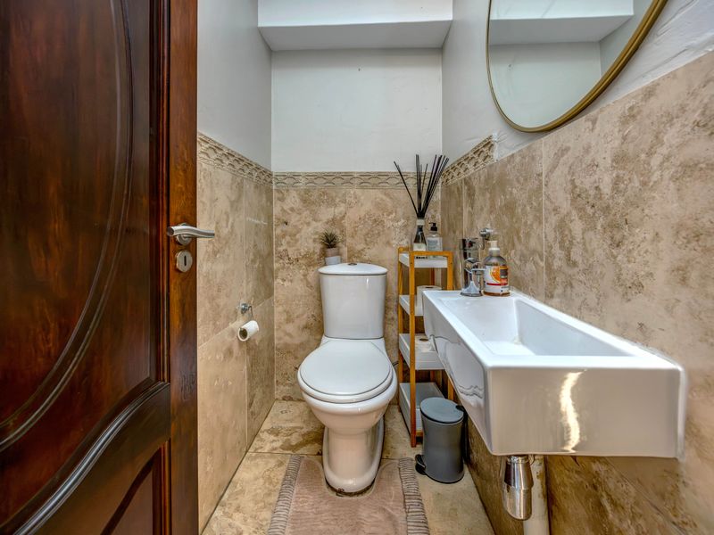 A compact guest bathroom featuring travertine wall and floor tiling, a modern wall-mounted basin, and a sleek chrome mixer tap.