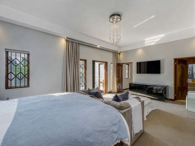 Spacious bedroom featuring a recessed ceiling with a crystal chandelier, carpeted flooring, and direct access to an outdoor area through timber doors.