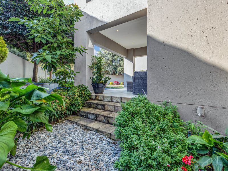 A covered patio area featuring stone steps leading from a landscaped garden with gravel pathways and established greenery.