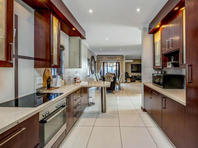Modern open-plan kitchen featuring dark wood cabinetry, stone countertops, integrated appliances, and a breakfast bar, flowing seamlessly into the dining and living areas.