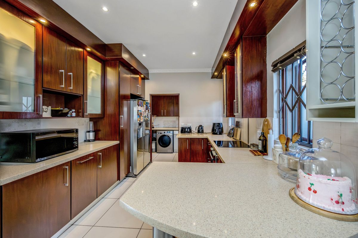 A well-maintained kitchen featuring dark wood cabinetry, stone countertops, integrated appliances, and tiled flooring with a functional layout and recessed lighting.
