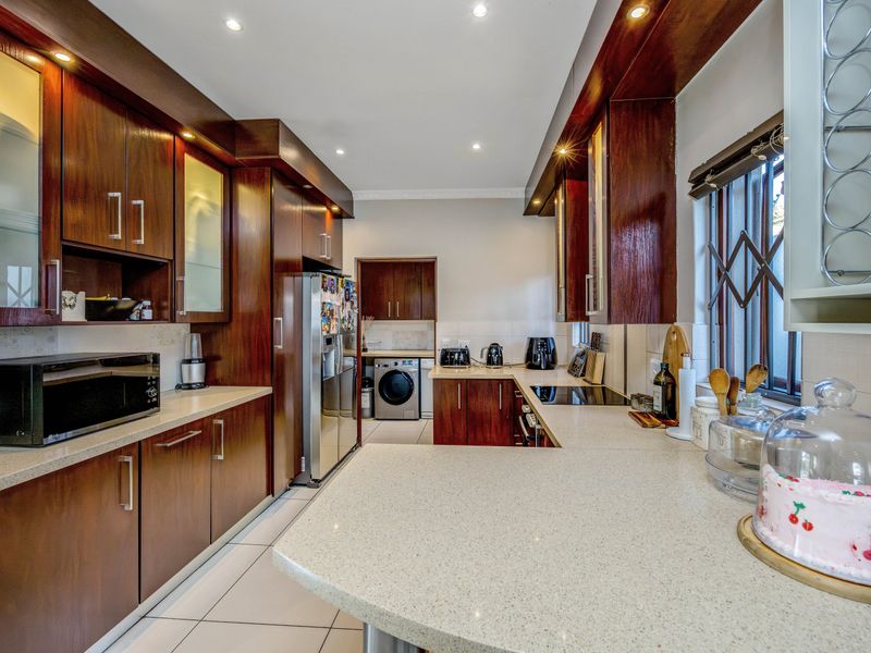 A well-maintained kitchen featuring dark wood cabinetry, stone countertops, integrated appliances, and tiled flooring with a functional layout and recessed lighting.