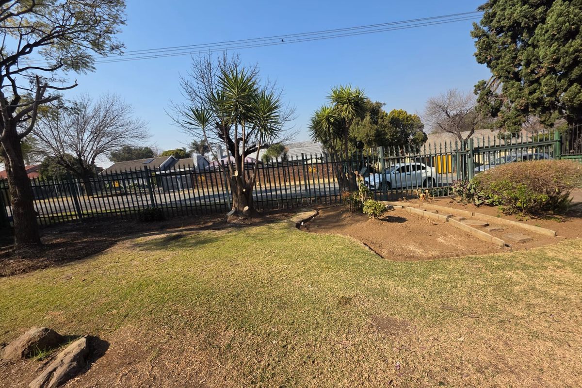 A view of the front garden area featuring established trees, landscaped garden beds, and secure metal perimeter fencing.