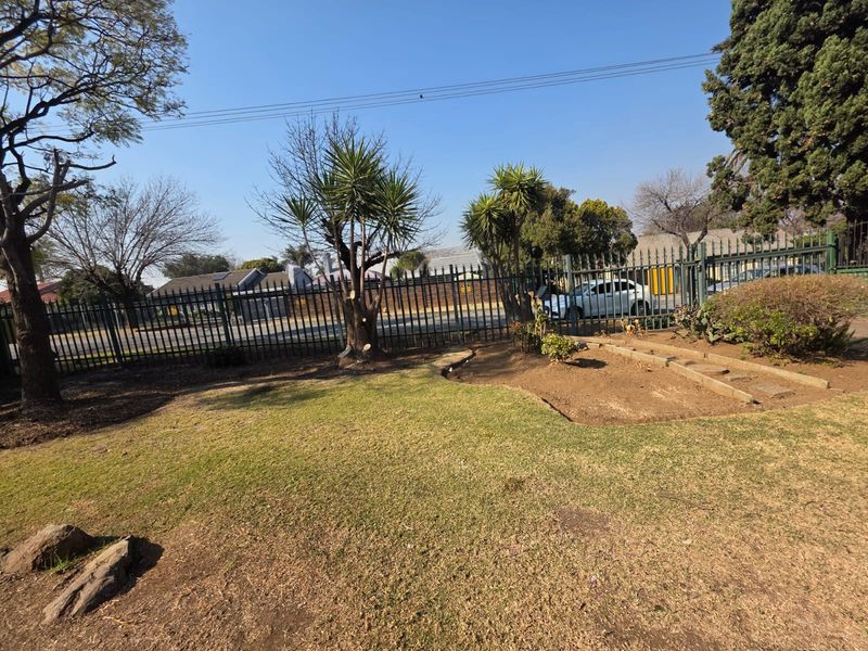 A view of the front garden area featuring established trees, landscaped garden beds, and secure metal perimeter fencing.