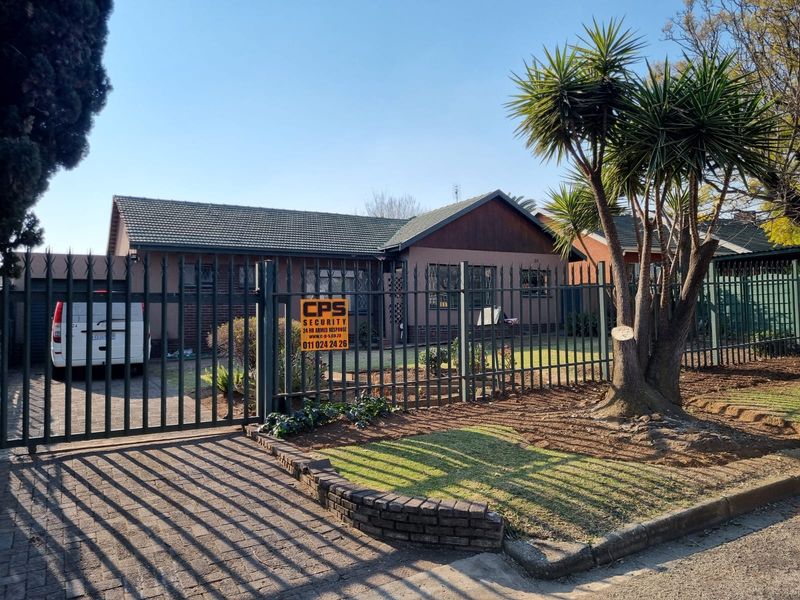 Front elevation of a residential house featuring a tiled roof, paved driveway, and secure metal perimeter fencing with a gated entrance.