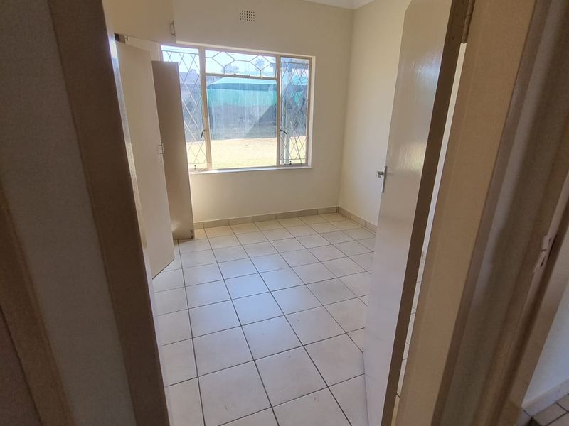 An empty bedroom featuring tiled flooring, built-in cupboards, and a window with security bars, offering a clean and functional space.