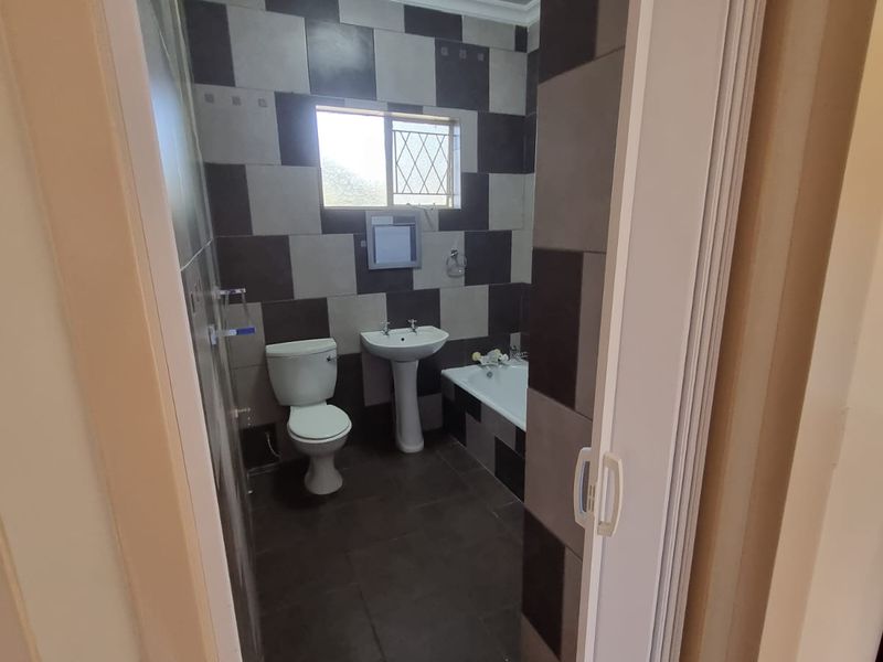 A functional bathroom featuring a pedestal basin, toilet, and bathtub with contrasting dark and light wall tiling.