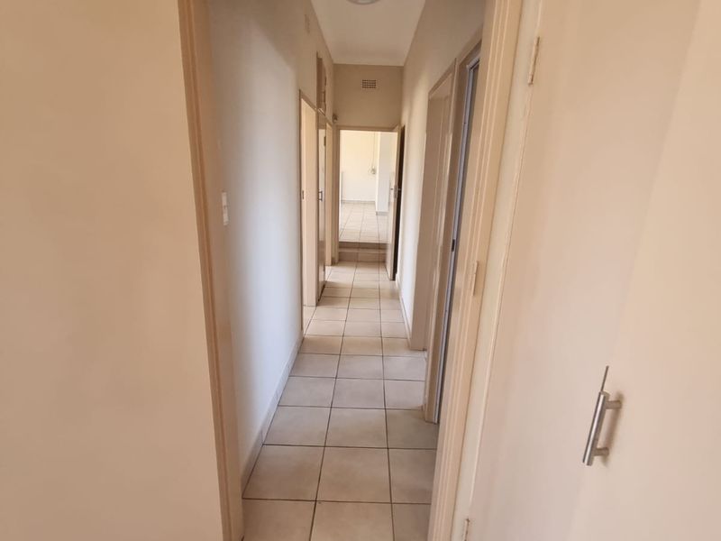 A clean, empty hallway featuring neutral tiled flooring and built-in storage cupboards, providing access to multiple rooms.