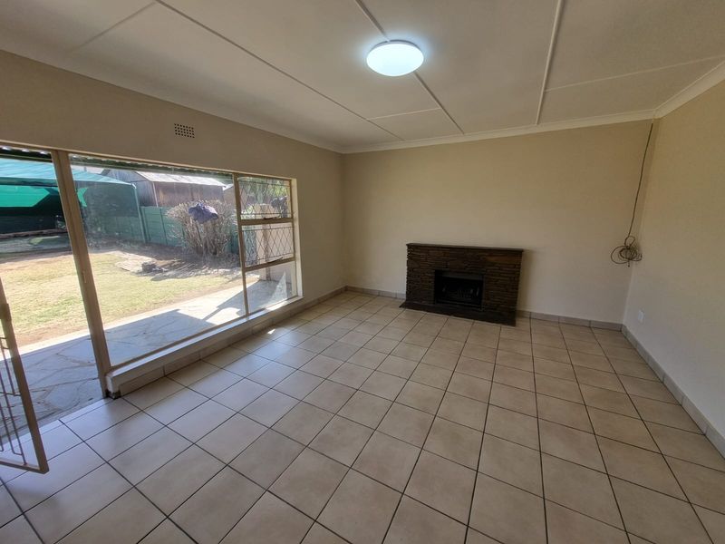 An empty living room featuring tiled flooring, a stone fireplace, and a large sliding glass door providing access to the rear garden.