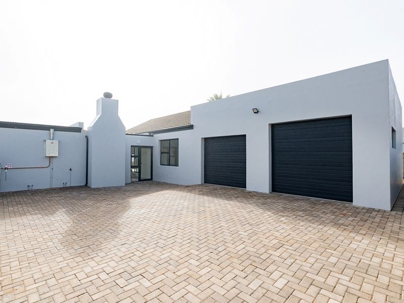 A clean exterior view of the property featuring a double garage, paved driveway, and a well-maintained facade with a gas geyser installation.