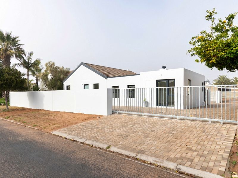 A modern, white-rendered single-story house featuring a paved driveway, secure metal sliding gate, and perimeter walling.