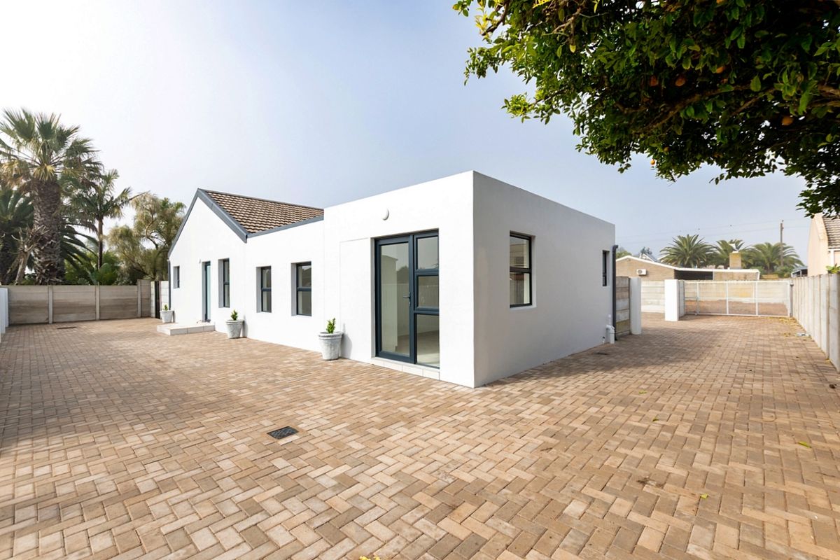 Rear view of a modern white house featuring paved courtyard, clean architectural lines, and dark aluminium window and door frames.