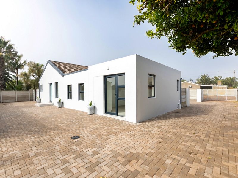 Rear view of a modern white house featuring paved courtyard, clean architectural lines, and dark aluminium window and door frames.
