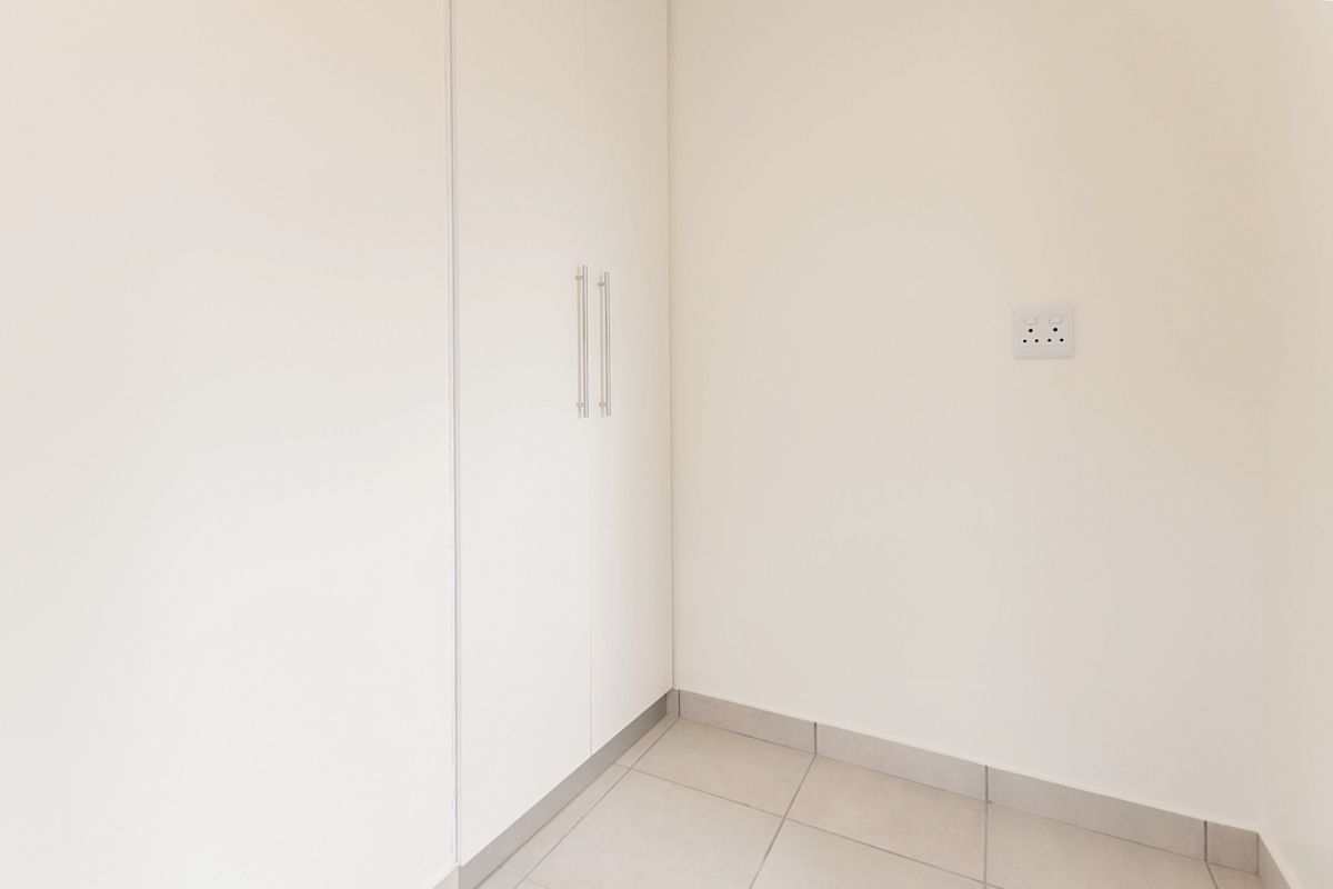 A clean, minimalist bedroom corner featuring neutral tiled flooring and white built-in cupboards with modern handles.
