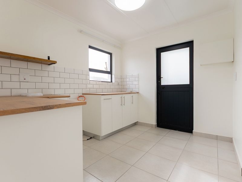 A clean, modern scullery featuring white cabinetry, wooden countertops, subway tile backsplash, and tiled flooring with direct access to the exterior.