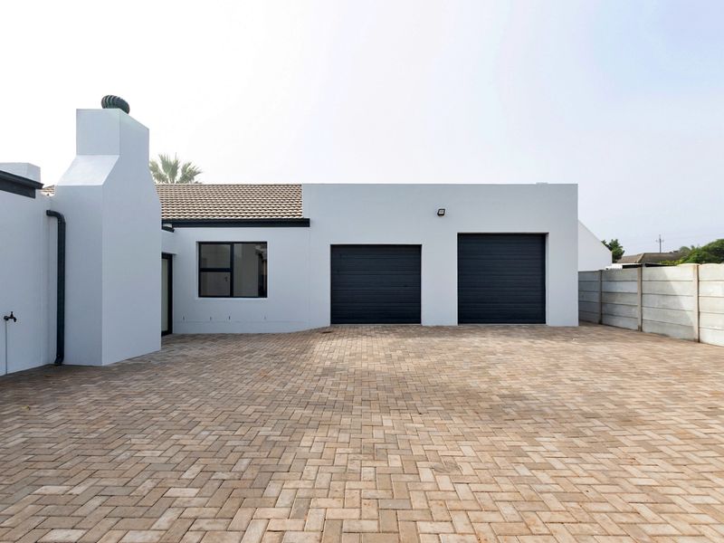 A clean front exterior view featuring a double garage, paved driveway, and a prominent external chimney on a well-maintained property.
