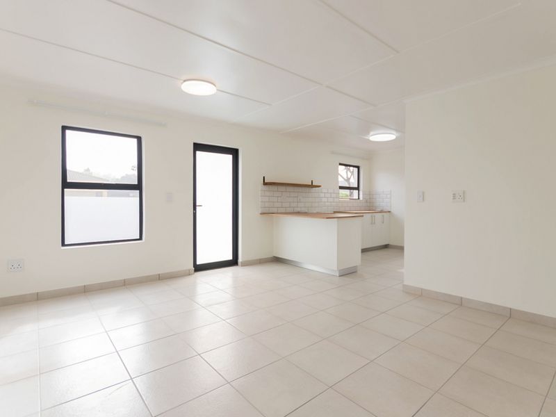A bright, open-plan living and kitchen area featuring neutral tiled flooring, modern cabinetry, and a functional kitchen island with a timber countertop.