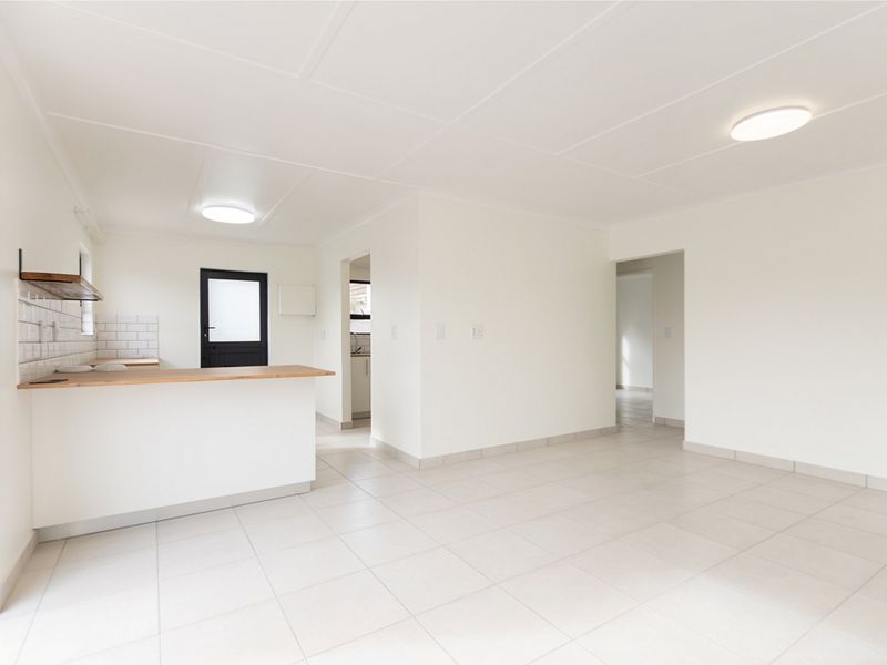 Bright and spacious open-plan living area featuring neutral tiled flooring, a breakfast bar with subway tile backsplash, and direct access to the exterior.