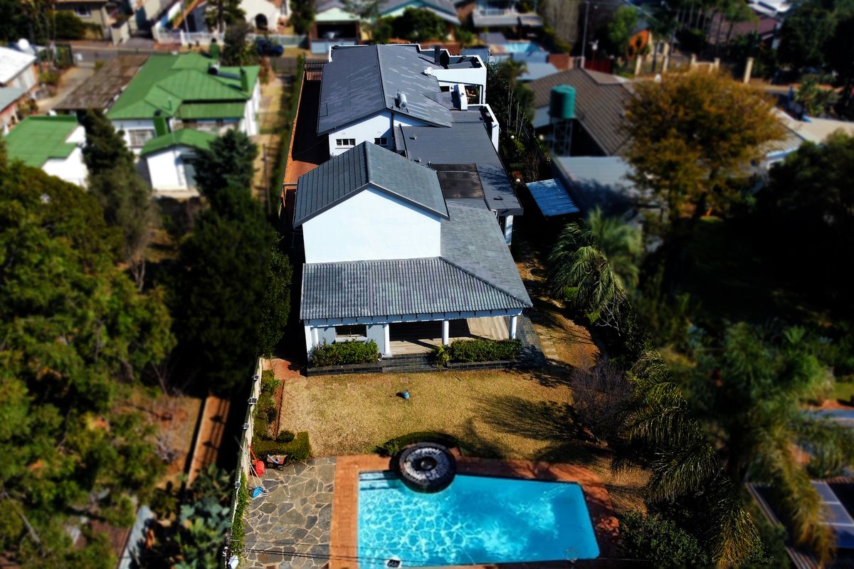 Aerial view of the property featuring a swimming pool, stone-paved patio area, and a multi-pitched tiled roof structure set within a residential garden.