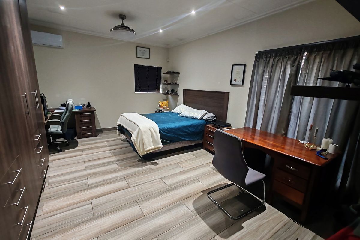 Spacious bedroom featuring modern wood-look tiled flooring, built-in cabinetry, a ceiling fan, and a split-system air conditioning unit.