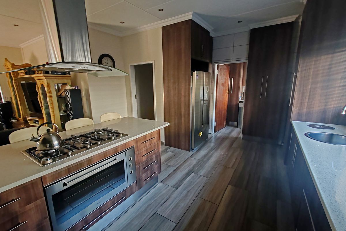 Modern kitchen featuring dark wood cabinetry, stone countertops, a central island with a gas hob and built-in oven, and wood-look tiled flooring.