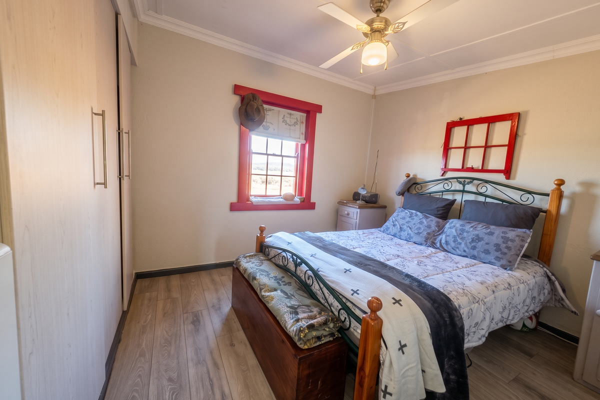 A cozy bedroom featuring laminate flooring, built-in cupboards, and a ceiling fan, with a bright window providing natural light.