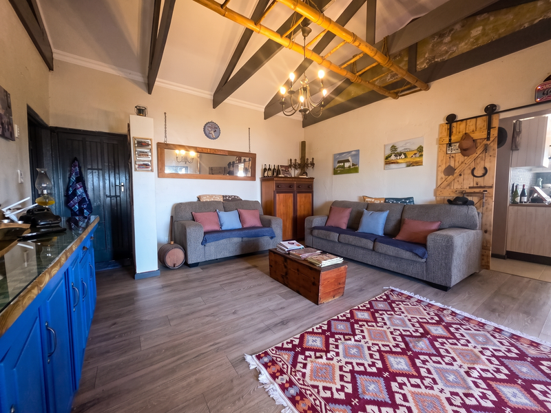 A rustic living room featuring a vaulted ceiling with exposed timber beams, laminate flooring, and a sliding barn door leading to an adjacent space.