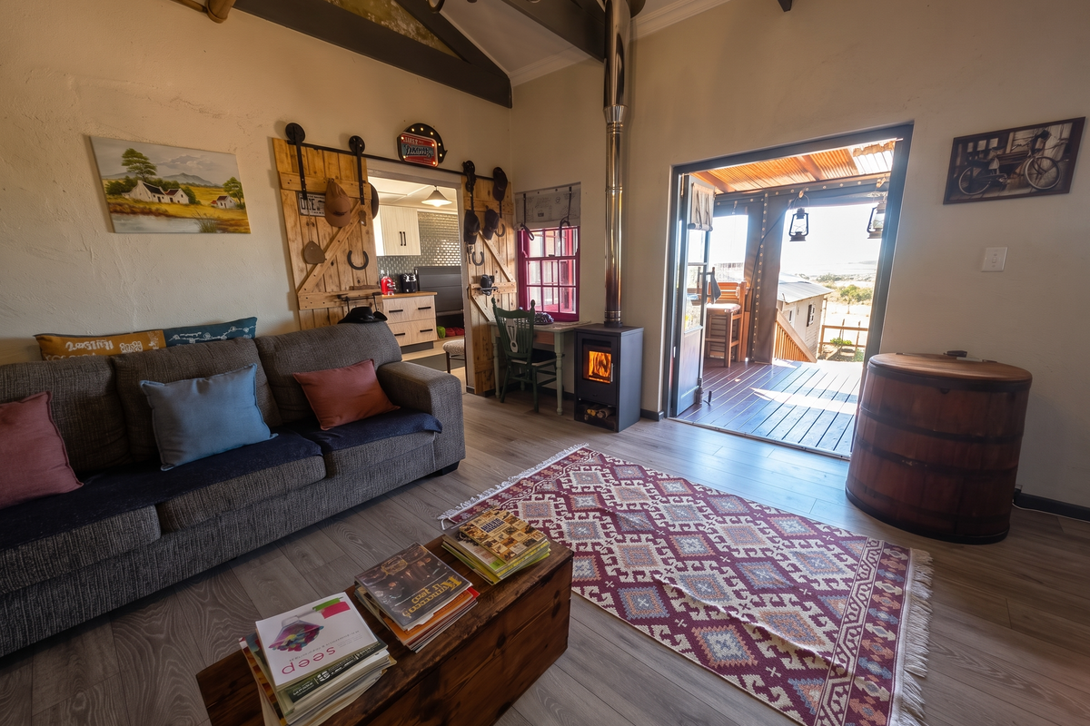 Cozy living room featuring a wood-burning fireplace, exposed timber beams, and direct access to an outdoor timber deck through a wide doorway.