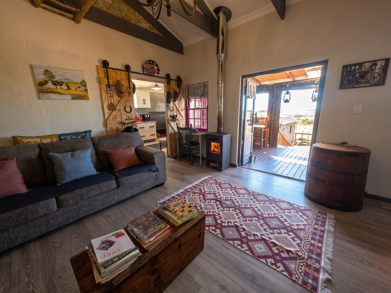Cozy living room featuring a wood-burning fireplace, exposed timber beams, and direct access to an outdoor timber deck through a wide doorway.