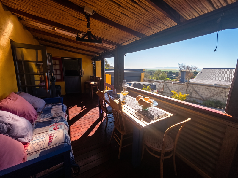 A covered outdoor patio featuring timber decking, a bamboo ceiling, and scenic views, providing a rustic space for relaxation and dining.
