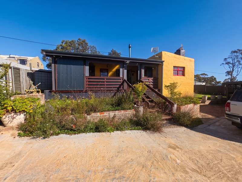 Front view of a house featuring a covered patio with timber decking, corrugated metal accents, and a concrete driveway.