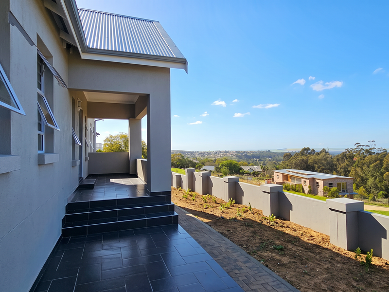 A covered patio area with dark tiled flooring, overlooking a landscaped garden and scenic neighbourhood views.