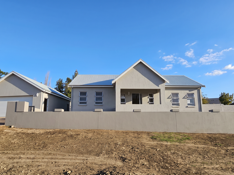 Front elevation of a modern single-story house featuring a corrugated metal roof, louvered windows, an attached garage, and a perimeter boundary wall.