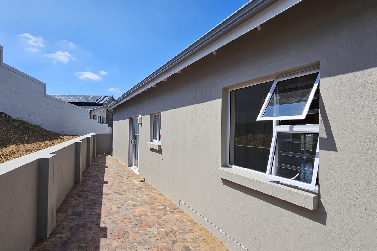 A side exterior view of the property featuring a paved walkway, retaining wall, and modern aluminium window frames.