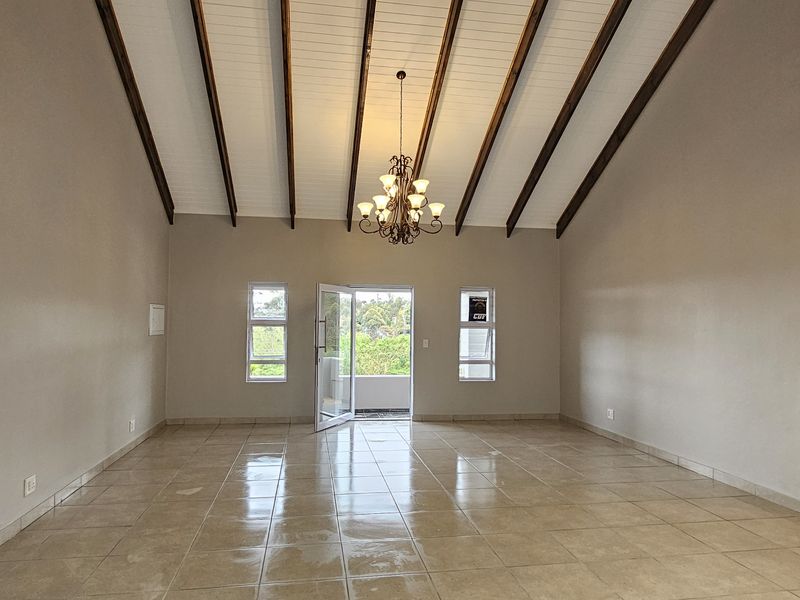 Spacious living area featuring a high vaulted ceiling with exposed timber beams, tiled flooring, and access to an outdoor balcony.