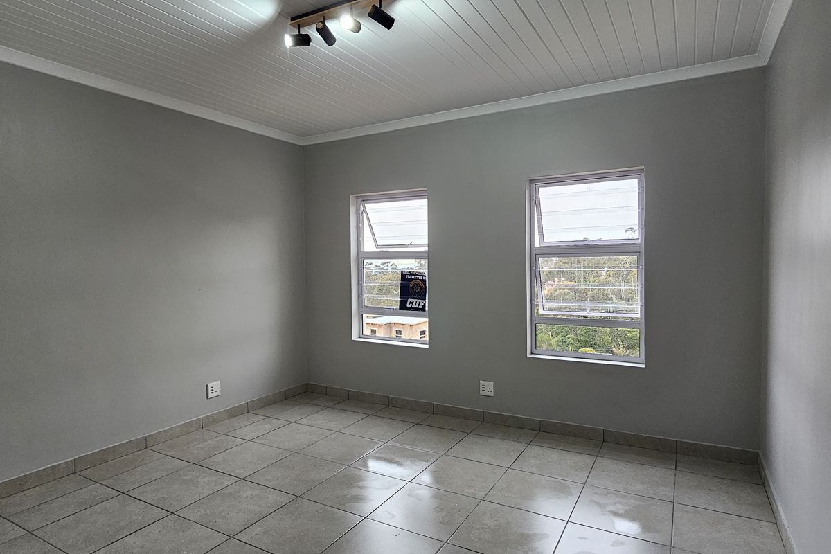 A bright, empty bedroom featuring neutral grey walls, tiled flooring, and a white tongue and groove ceiling with modern track lighting.