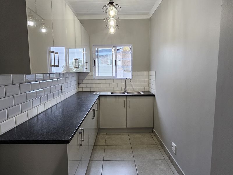 A clean and modern scullery featuring sleek cabinetry, dark countertops, a stainless steel double sink, and a classic subway tile backsplash.