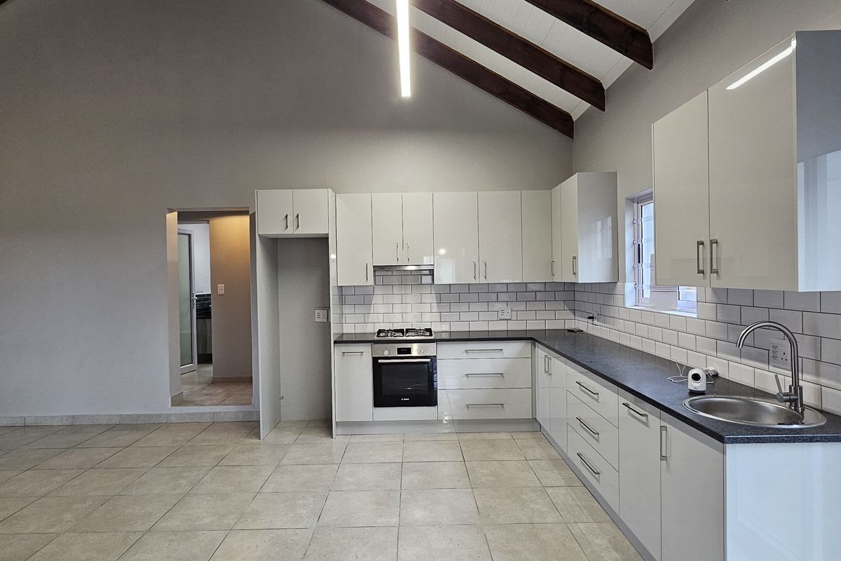 Modern open-plan kitchen featuring high-gloss cabinetry, subway tile backsplash, built-in oven, gas hob, and vaulted ceilings with exposed timber beams.