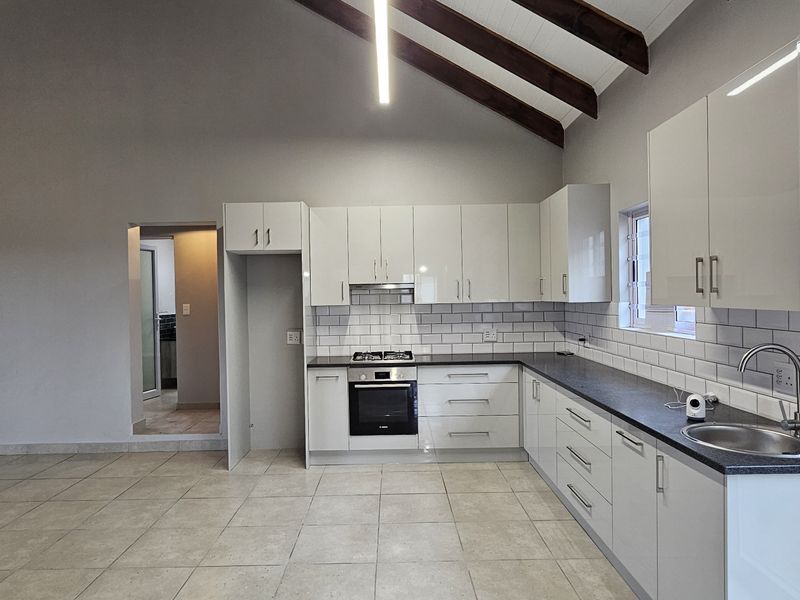 Modern open-plan kitchen featuring high-gloss cabinetry, subway tile backsplash, built-in oven, gas hob, and vaulted ceilings with exposed timber beams.